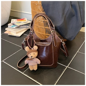 Detail of dark brown glossy bucket bag with a cute bear plush charm and adjustable strap