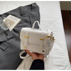 Detail of white PU leather square bag with gold metal clasp on a grey suit jacket