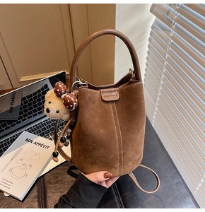 Detalle de bolso cubo marrón mate con colgante de osito en un entorno de estilo de vida