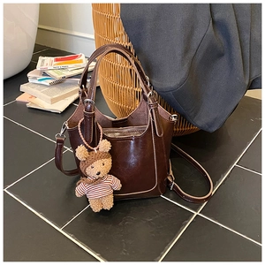 Detail of dark brown bucket bag with smooth finish and cute plush bear charm accessory