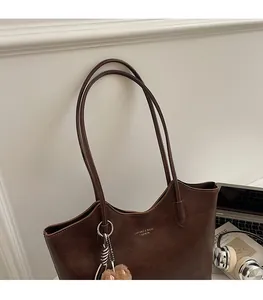 Deep brown retro leather tote bag with gold logo and plush charm in a chic setting