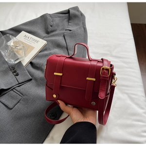 Detail of red vintage PU leather crossbody bag with dual straps and gold metal buckle