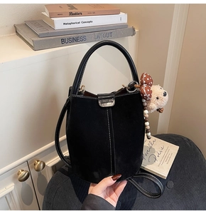 Detalle de bolso tipo cubo en ante negro con hebilla metálica y amuleto de osito