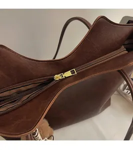 Close-up of golden zipper on dark brown tote bag with striped lining and plush ball charm