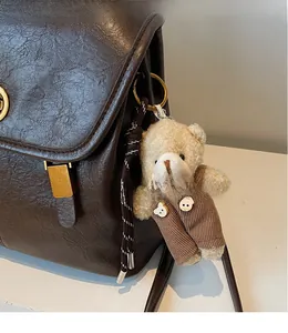 Close-up of a plush teddy bear bag charm with corduroy overalls on a leather backpack