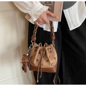 Detalle de bolso saco marrón con bordado floral, asa trenzada y un lindo colgante de oso