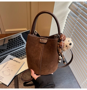 Detalle del bolso de cubo en cuero esmerilado marrón oscuro con colgante de oso de peluche