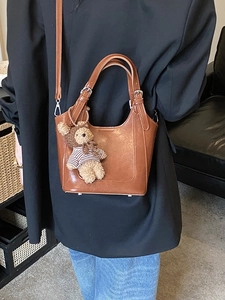 Retro brown bucket bag with plush bear charm worn with a black blazer and denim