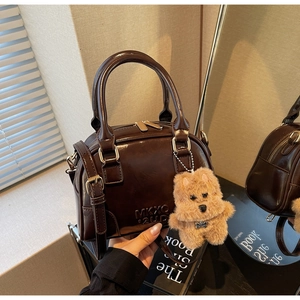 Detail of glossy brown Boston bag with MKXO 2UP embossing and cute bear keychain
