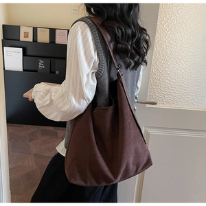 Close-up of a large coffee brown faux suede bucket bag worn over the shoulder