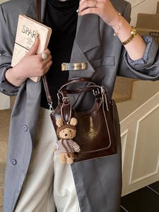 Fashionable dark brown oily leather bucket bag with a plush bear charm worn by a model
