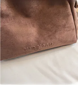 Détail du sac bandoulière en daim marron avec texte CHRS'2AD embossé sur la peau