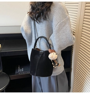 Detalle del bolso de ante negro con costuras blancas y colgante de oso de peluche suave