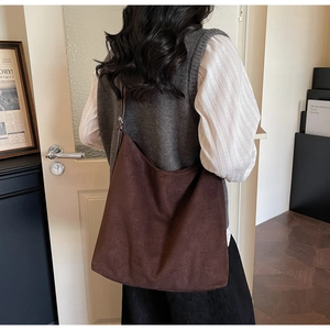 Detail of a large dark brown matte suede shoulder bag worn by a model in a cozy setting
