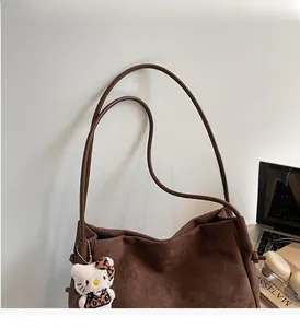 Détail d'un sac cabas en daim marron avec de longues anses et un charm en peluche