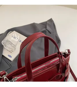 Detail of deep red patent leather handbag with silver zipper and sturdy top handles