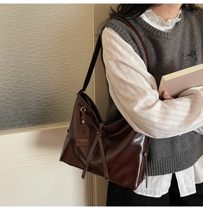 Detail of dark brown glossy leather tote bag with decorative strap and metal ring