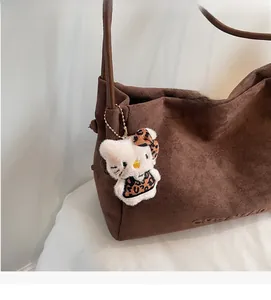 Détail du cabas en daim marron foncé avec bandoulière en cuir et charm chat en peluche