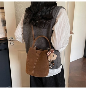 Detalle del bolso tipo cubo en ante marrón con costuras y colgante de osito de peluche