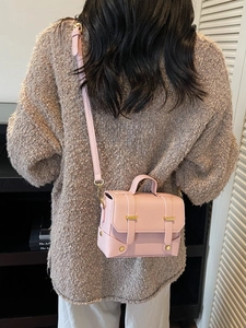 Minimalist light pink square crossbody bag with gold buckles worn by a model