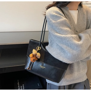 Dettaglio della borsa tote nera in pelle con un simpatico ciondolo a forma di orsetto