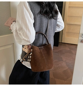 Detalle del bolso tipo cubo de ante marrón con costuras blancas y colgante de osito