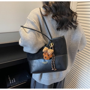 Dettaglio della borsa tote nera con ciondolo a cucciolo di peluche e texture del tessuto