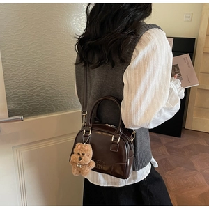 Detail of dark brown patent leather bowling bag with cute plush bear charm accessory