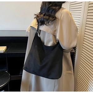 Detail of a large black suede hobo shoulder bag shown on a model in a long trench coat