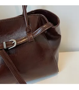 Detail of dark brown glossy leather tote with silver metal buckle and fine stitching