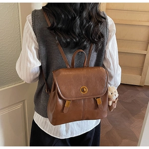 Rear view of a vintage brown PU leather backpack with a plush bear charm on a model