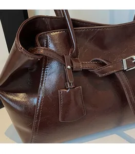 Detail of deep brown glossy leather tote bag with stylish charm and metallic buckle strap