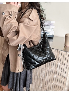 Close-up of black quilted hobo bag with silver chain strap worn with a camel trench coat