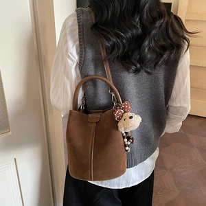 Bolso cubo retro de ante marrón oscuro con asa y amuleto de oso llevado por una modelo