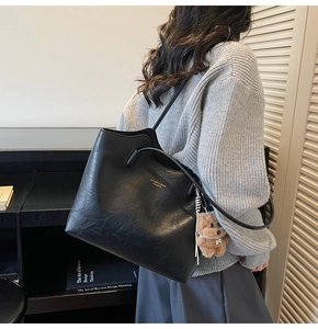 Detail of black faux leather tote bag with gold lettering and brown plush bear charm