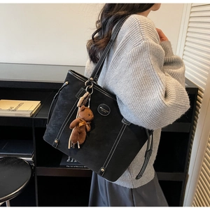 Detail of black suede tote bag with white stitching and cute teddy bear charm