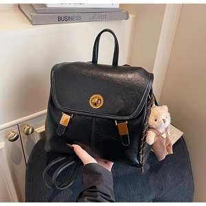 Close-up of black retro leather backpack with gold buckle and plush bear charm