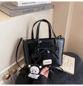 Detail einer schwarzen PU-Leder-Eimertasche mit Schleife und weißem Katzenanhänger