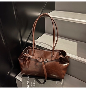 Detail of vintage brown glossy leather tote bag showing refined texture and buckle strap