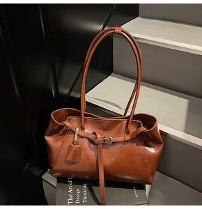 Detail view of brown faux leather tote with slim handles and silver buckle on black books