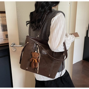 Detail of dark brown leather tote bag with white stitching and plush bear charm