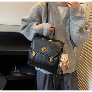 Detail of vintage black leather backpack with gold rotary lock and plush bear pendant