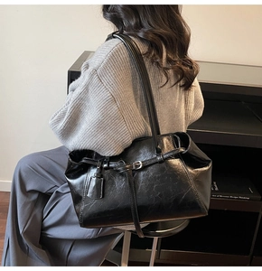 Detail of black glossy tote bag featuring vintage pleated texture and buckle decoration