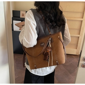 Brown leather tote bag with plush bear charm worn by a model in a cozy cafe setting