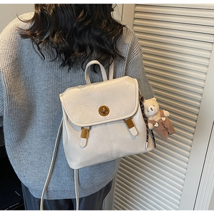 Detail view of a vintage beige backpack with gold hardware and a cute bear charm accessory
