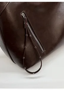 Macro shot of dark brown leather handbag featuring silver zipper and rivet strap detail