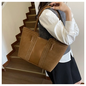 Detail of a large brown tote bag featuring white contrast stitching and woven side accents