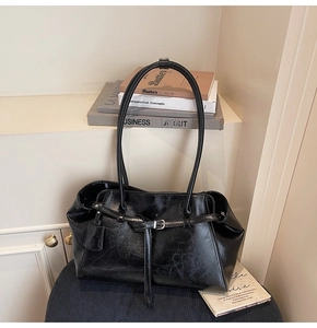 Detail of glossy black leather tote bag featuring slim straps and metal buckle accents