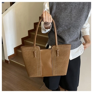 Detail of a brown leather tote bag with white contrast stitching and woven leather accents