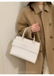 Detail of white crocodile pattern tote bag with top handle worn on a camel coat